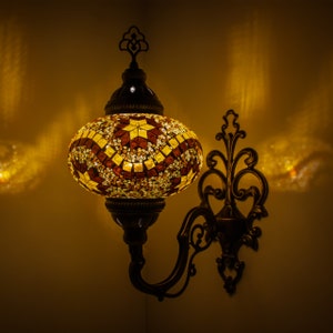 May include: A wall-mounted mosaic glass lamp with a decorative metal arm. The lampshade is round and features a geometric pattern in shades of brown, yellow, and white.