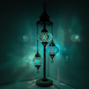 May include: A three-light floor lamp with a traditional design. The lamp has a metal base and three blue glass globes with intricate mosaic patterns. The globes are illuminated with warm white light.