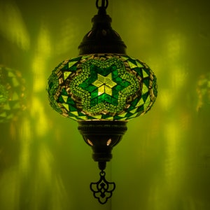 May include: A green and white mosaic glass pendant light with a star pattern. The light is hanging from a chain and has a metal frame.