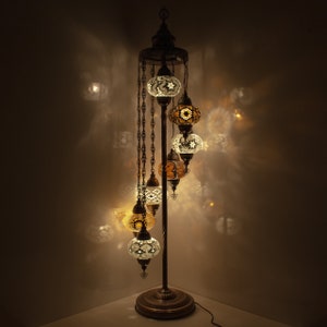 May include: A floor lamp with a spiral design and six mosaic glass globes. The globes are in shades of white, gold, and amber. The lamp is lit and casting a warm glow.