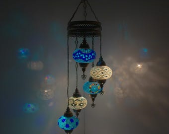 May include: A multi-tiered chandelier with five mosaic glass globes. The globes are in shades of blue and white, with intricate patterns. The chandelier is suspended from a chain and has a metal frame.