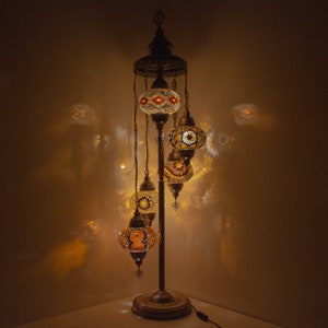 May include: A floor lamp with a gold metal base and five hanging glass globes. The globes are decorated with colorful mosaic tiles and emit a warm glow.