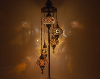 May include: A floor lamp with a gold metal base and five hanging glass globes. The globes are decorated with colorful mosaic tiles and emit a warm glow.