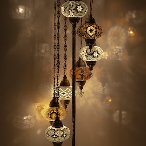 May include: A floor lamp with multiple hanging glass globes. The globes are made of mosaic tiles in shades of white, gold, and brown. The lamp is a decorative piece for a home.