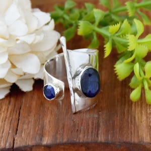 以下が含まれることがあります： 2つの青い宝石が付いた銀の指輪。指輪は開いていて調節可能です。指輪はハンマーで叩いた銀でできており、ユニークなデザインです。