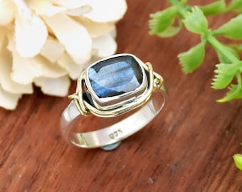 Op de afbeelding: Een zilveren ring met een blauwe labradorit edelsteen gezet in een gouden draad gewikkelde bezel. De ring is gemarkeerd met het nummer "925" aan de binnenkant van de band.