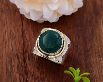 May include: A silver ring with a green gemstone set in a gold bezel. The ring has a hammered texture.