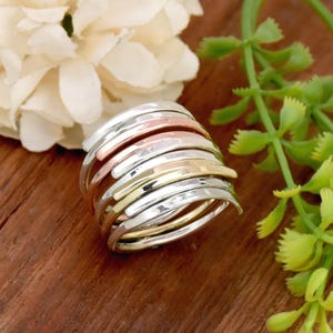 May include: A stack of thin, hammered metal rings in silver, gold, and copper tones. The rings are stacked on top of each other and are arranged in a staggered pattern.