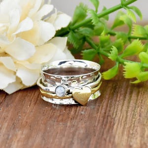 Puede incluir: Un anillo giratorio de plata y oro con una piedra de ópalo blanco y un dije en forma de corazón.