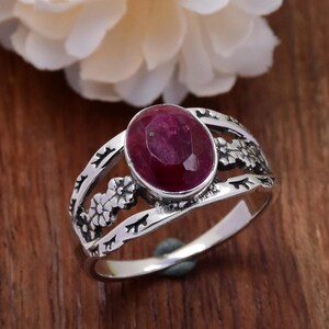 Peut inclure: Une bague en argent avec une pierre précieuse en rubis rouge sertie dans un motif floral.