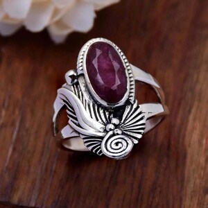 May include: A silver ring with a large, oval-shaped, dark red gemstone set in a detailed, ornate design.