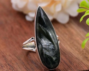 May include: A silver ring with a teardrop-shaped black and green gemstone. The gemstone has a shimmering, iridescent effect.
