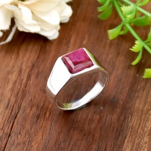 May include: A silver ring featuring a square, deep red gemstone. The ring has a polished finish and a classic design. The gemstone is set in a bezel setting. Suitable for everyday wear or special occasions.