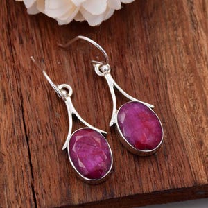 Puede incluir: Un par de pendientes colgantes de plata con piedras preciosas de rubí rosa de forma ovalada.