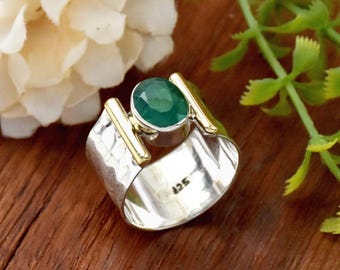 May include: A silver ring with a hammered texture and gold accents. A large green gemstone is set in the center of the ring.