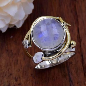 May include: A silver ring with a gold band and a large oval moonstone. The ring has a delicate design with a small butterfly detail.