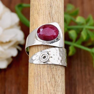 Puede incluir: Un anillo de plata con acabado martillado y una piedra preciosa roja. El anillo está diseñado para envolverse alrededor del dedo.