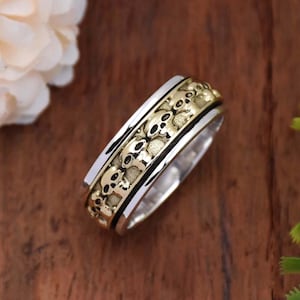 May include: A silver and gold spinning ring with a design of multiple skulls around the band.