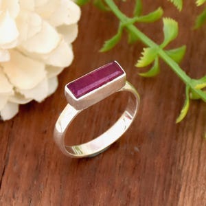 May include: A silver ring with a rectangular, dark purple gemstone set in the center.