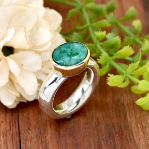 May include: A silver ring with a green emerald gemstone set in a gold band.
