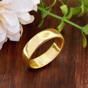 May include: A gold wedding band with a smooth, rounded surface. The band is about 6mm wide and has a subtle shine.