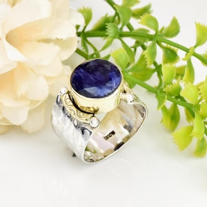 May include: A silver and gold ring with a blue gemstone. The ring has a textured band and a round bezel setting.