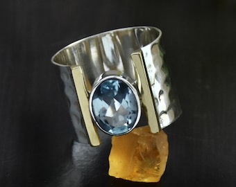 May include: A silver ring with a blue gemstone set in a gold band. The ring is hammered and has a textured finish.