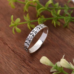 Puede incluir: Un anillo de plata con un diseño floral. El anillo es fino y delicado, y las flores son en relieve y detalladas.