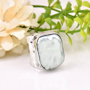 May include: A silver ring with a large, white, rectangular pearl. The ring has a textured band.