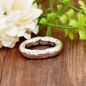 Może przedstawiać: Srebrny pierścionek z fakturowanym, młotkowanym wykończeniem. Pierścionek jest gruby i ma zaokrąglony kształt.