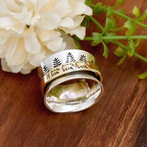 Peut inclure: Une bague tournante en argent et or avec un motif d'arbres et d'ours. La bague est posée sur une surface en bois.