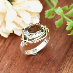 May include: A silver and gold ring with a light green gemstone. The ring has a twisted wire design.