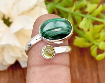 May include: A silver ring with a green malachite oval gemstone and a smaller yellow gemstone. The ring is on a finger.