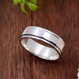 Puede incluir: Un anillo de plata con un diseño acanalado. El anillo es liso y brillante.
