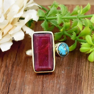 May include: A gold ring featuring a large rectangular red gemstone and a smaller round turquoise gemstone.