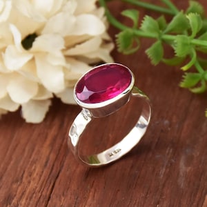 May include: A silver ring featuring a large, oval-shaped, deep pink gemstone. The ring has a hammered texture.