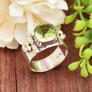 Puede incluir: Un anillo de plata con una gran piedra preciosa verde y detalles dorados. El anillo está estampado con "925" en la banda interior.