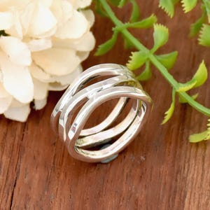 Puede incluir: Un anillo de plata con un diseño único y de múltiples capas. El anillo está hecho de tres bandas que están entrelazadas y tienen una textura ligeramente martillada.