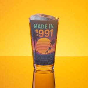 May include: A pint glass filled with beer and foam, featuring a retro design with a sunset, palm trees, and the text "MADE IN 1991". The glass is clear, and the background is a solid yellow.