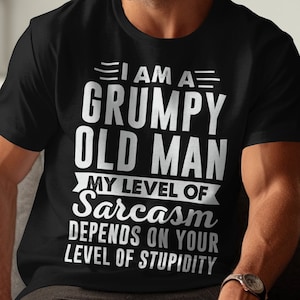 May include: A black short-sleeved t-shirt featuring white text that reads: I AM A GRUMPY OLD MAN MY LEVEL OF Sarcasm DEPENDS ON YOUR LEVEL OF STUPIDITY. The shirt has a crew neckline and a standard fit, displaying bold, capitalised lettering.