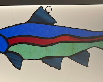 May include: A stained glass fish with blue, green, and red colors. The fish has a black outline and a white circle at the top.