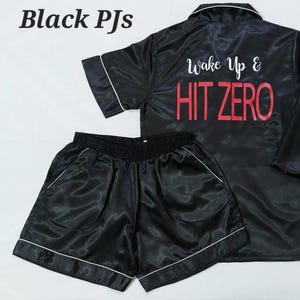 May include: Black satin pyjama set with white trim. The top has "Wake Up & HIT ZERO" printed on the back. The shorts have a white trim and the bottom of the shirt has "WCHS Cheer" printed on it.