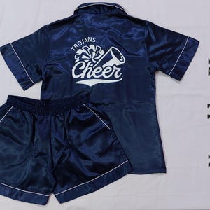 May include: Navy blue satin pyjama set with a white "Trojans Cheer" graphic on the top. The shorts have a white trim.