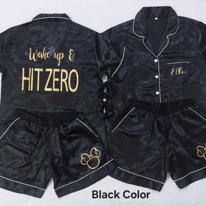May include: Black satin pajama set with gold embroidery. The top has short sleeves and a button-up collar. The shorts have a drawstring waist and a Mickey Mouse design. The text "Wake up & HIT ZERO" is embroidered on the top.