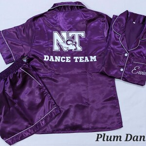 May include: Purple satin pyjamas with a white "NT Dance Team" logo on the top and "Eunice" embroidered on the bottom.