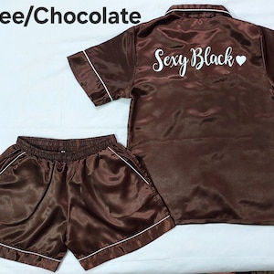 Könnte beinhalten: Ein braunes Satin-Pyjama-Set mit kurzen Ärmeln und Shorts. Das Oberteil hat "Sexy Black" in weiß mit einem weißen Herzen auf der Rückseite gestickt.