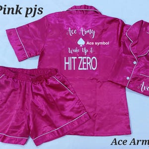 May include: Hot pink satin pyjamas with short sleeves and shorts. The top has the text "Ace Army" with a spade symbol and the text "Wake Up & HIT ZERO". The shorts have a white trim.
