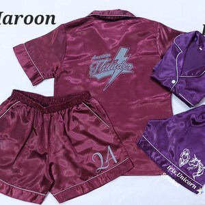 May include: Two sets of satin pyjamas in maroon and plum. The maroon set features the number 24 on the shorts and "American Thunder" on the shirt. The plum set has a unicorn design and the text "Iris, Unicorn, Sentinel".
