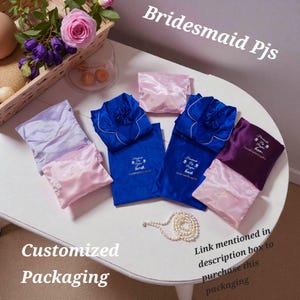 May include: Bridesmaid PJs in various colors, including blue, purple, and pink, are displayed on a white table. Each set is neatly packaged in a matching satin pouch. The text "Customized Packaging" is visible.