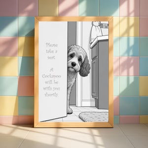 May include: A monochrome framed print showing a Cockapoo dog looking out from behind a door. The text on the frame says, "Please take a seat. A Cockapoo will be with you shortly."